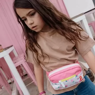 Menina com pochete rosa, camiseta bege e calças de ganga em ambiente interior