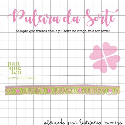 Pulseira da Sorte com estampa LUCKY e trevo de quatro folhas rosa num fundo quadriculado.