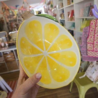 Prato em forma de fatia de limão amarelo e verde segurado por mão com unhas rosa claro em loja