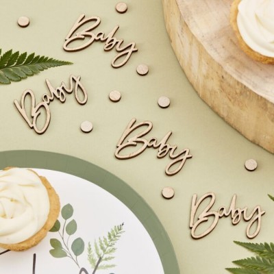 Recortes em madeira da palavra 'Baby' em fonte cursiva, folhas verdes e cupcakes com cobertura branca