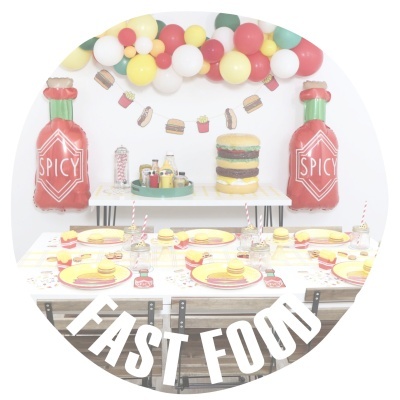 Decoração de festa temática fast food com balões, bolo hambúrguer e mesas postas.