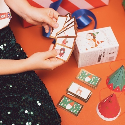 Mãos segurando cartas de jogo natalícias com motivos festivos em fundo laranja