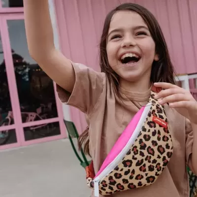 Menina sorridente com mala de cintura com padrão animal print e interior rosa