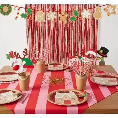 Mesa de Natal decorada com pratos, copos, canudos e acessórios festivos em vermelho, rosa e motivos natalícios.