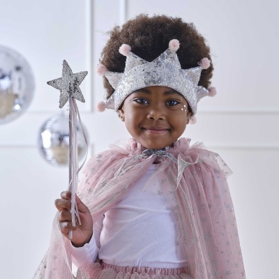 Criança com coroa prateada e capa cor-de-rosa segurando varinha de estrela