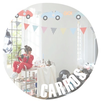 Criança vestida de vermelho perto de mesa com toalha branca e decoração colorida, balões e letras 'CARROS' no chão