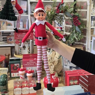 Boneco elfo de Natal com roupa vermelha e calças às riscas num ambiente decorativo de Natal