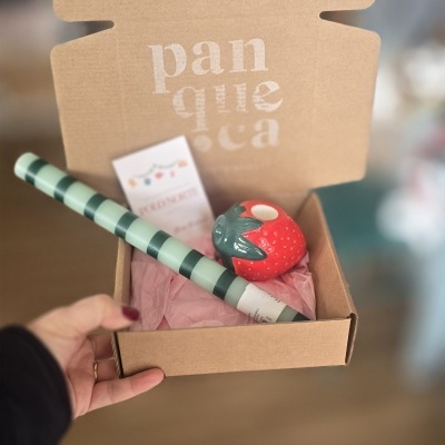 Caixa de cartão castanho aberta com itens dentro, incluindo uma mangueira riscada e um objecto vermelho semelhante a morango