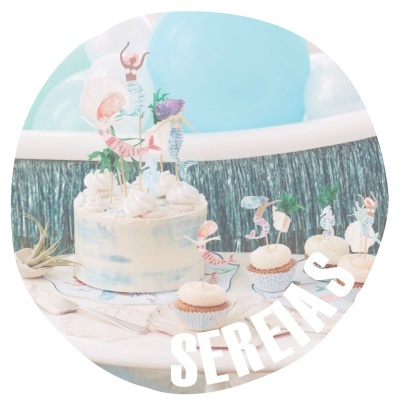 Bolo e cupcakes decorados com tema de sereias em mesa de festa com balões ao fundo
