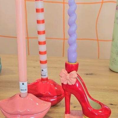 Três castiçais coloridos com velas em formato de lábios e sapato de salto alto.