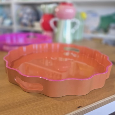 Tabuleiro plástico alaranjado com bordas onduladas e pegas laterais numa mesa de madeira.
