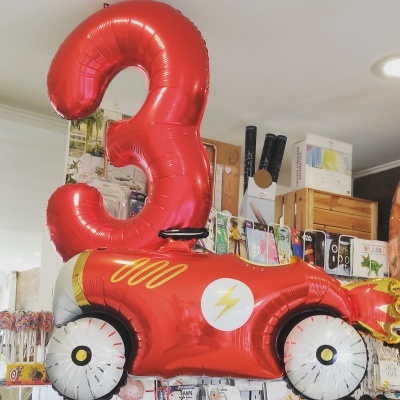 Balão de número 3 vermelho e balão de carrinho vermelho com detalhes amarelos e brancos em loja