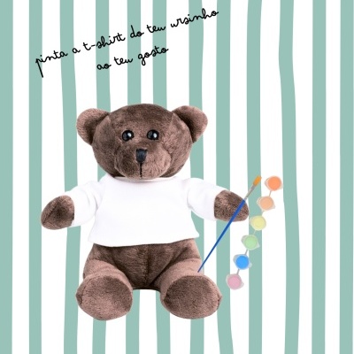 Urso de peluche com camisola branca e tintas para pintar, fundo riscas verdes e brancas