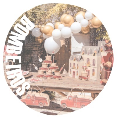 Mesa decorada para festa infantil com bolo, casinha de bonecas, balões brancos e dourados e sacos de papel com carrinha de bombeiros