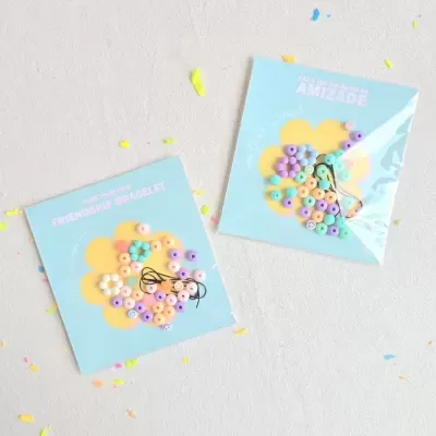 Dois conjuntos de pulseiras coloridas para amizade em embalagens com cartões azuis e confetes no fundo