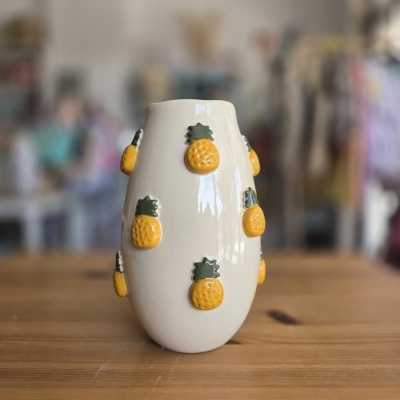 Vaso cerâmico branco com abacaxis amarelos em relevo sobre mesa de madeira
