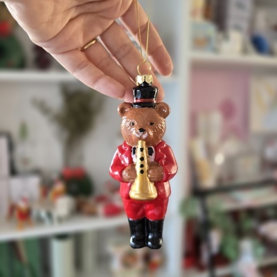 Ornamento de urso castanho com chapéu e roupa vermelha segurando saxofone dourado, suspenso por corrente dourada