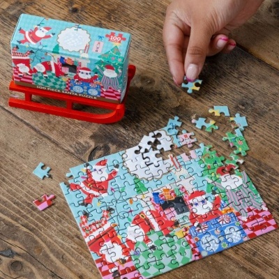 Puzzle de Natal com 100 peças, mostra Papai Noel, presentes coloridos, montado numa mesa de madeira