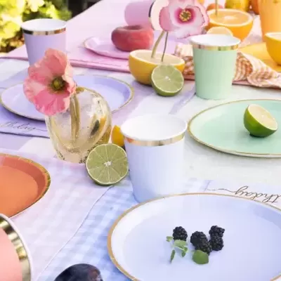 Utensílios de mesa coloridos com detalhes dourados em mesa decorada com flores e frutas