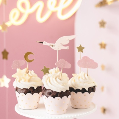 Três cupcakes decorados com coberturas brancas e toppers temáticos num suporte branco, com fundo rosa e estrelas douradas pendentes.