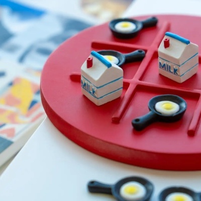 Jogo da velha com peças de leite e ovos em frigideiras sobre tabuleiro vermelho