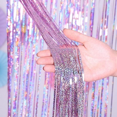Mão a segurar fitas de tinsel brilhantes e translúcidas cor roxo-rosa com brilho holográfico.