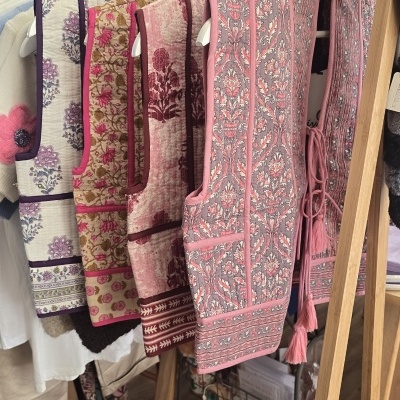 Coleção de coletes florais em tons rosa e vinho pendurados em estrutura de madeira