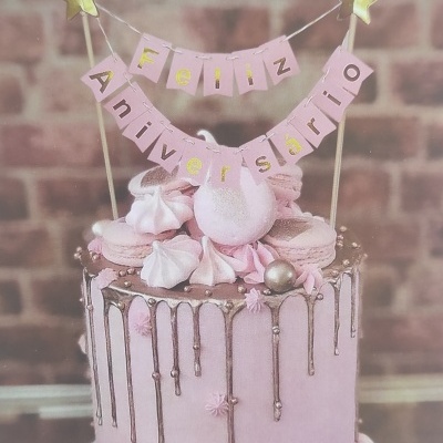 Bolo cor-de-rosa com decoração em chocolate e topos de festa com placa FELIZ ANIVERSÁRIO