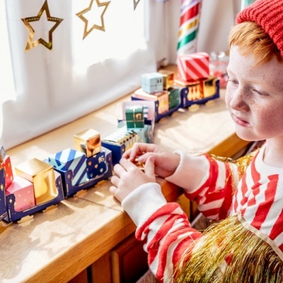 Criança com camisola riscada e gorro vermelho a brincar com comboio de madeira