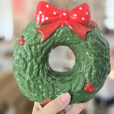 Figura decorativa de cerâmica verde com laço vermelho e pontos brancos, segurada por mão feminina
