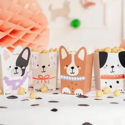 Caixas de papelão com desenhos de cães contendo pipoca numa mesa decorada com confetes e adornos de papel