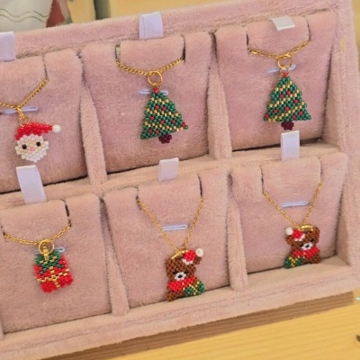 Colares com pendentes de contas em forma de Pai Natal, árvore de Natal, prenda e urso, exposição em almofada rosa.