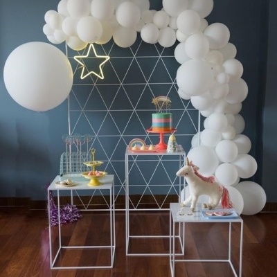 Decoração de festa com balões brancos em arco e mesa com bolo e unicórnio