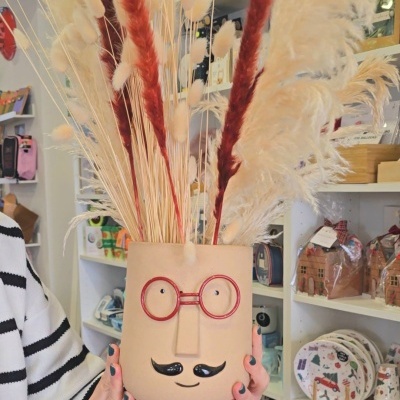 Vaso de cerâmica decorativo em formato de rosto com plantas secas