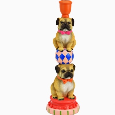 Estátua de dois cães pug decorativos, coloridos, numa bola e base redonda, com um copo laranja no topo.
