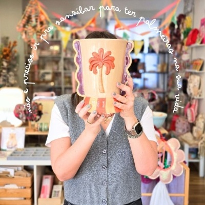 Vaso cerâmico colorido com desenho de palmeira segurado por pessoa em loja