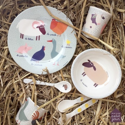 Conjunto de loiça infantil decorado com animais da quinta sobre palha.