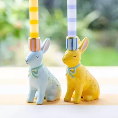 Dois castiçais de cerâmica em forma de coelhos coloridos com velas às riscas.