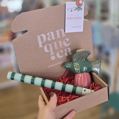 Caixa de cartão com ornamento de pássaro cerâmico e cilindro listrado, com etiqueta de entrega do Polo Norte.