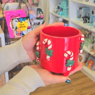 Caneca vermelha de cerâmica com bengalas de Natal em relevo segurada por mãos