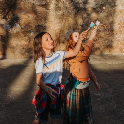 Duas crianças a brincar ao ar livre com brinquedos de madeira, parede de pedra ao fundo