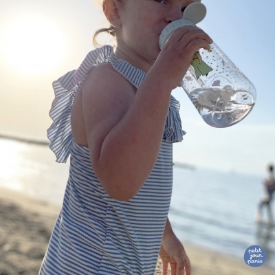 Criança com vestido às riscas a beber de garrafa na praia