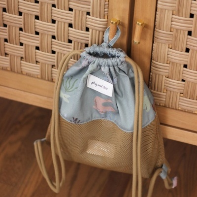 Mochila saco azul claro com padrões e parte inferior em rede cinzenta pendurada em móvel de madeira