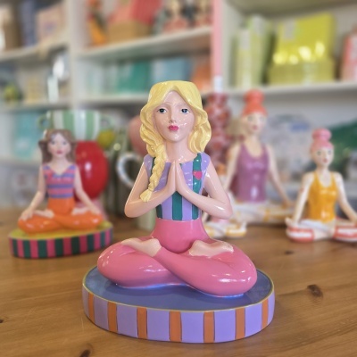 Figurine de mulher a fazer yoga vestida de rosa e roxo sentada em posição de lótus.