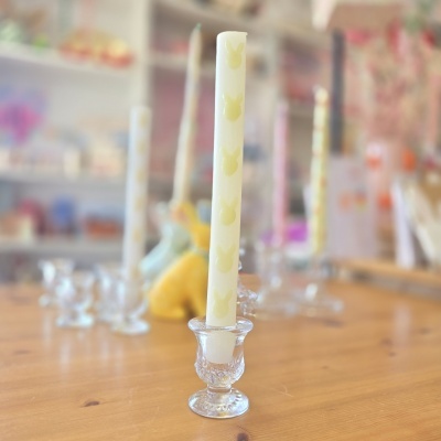 Velas brancas com estampas de coelho em castiçais de vidro numa mesa de madeira