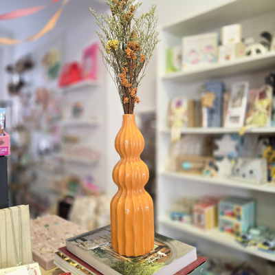 Vaso cerâmico laranja com ramo seco e flores colocados sobre livros num espaço interior