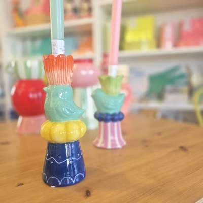 Dois castiçais de cerâmica coloridos com velas em cima de mesa de madeira.