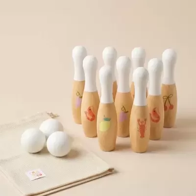 Conjunto de bowling infantil com pinos de madeira pintados e bolas brancas sobre saco de tecido.