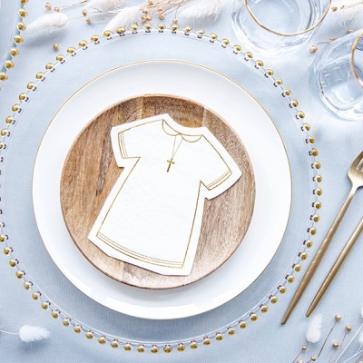 Conjunto de louça com prato branco e dourado, prato de madeira, decoração vestido e crucifixos dourados, talheres dourados e flores brancas sobre tela azul