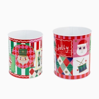 Duas latas decorativas natalícias coloridas com desenhos de soldado, Pai Natal, tambores e a palavra Jolly.